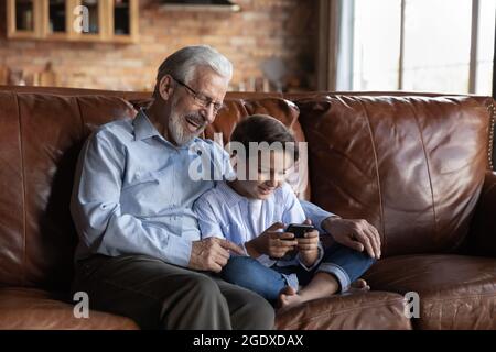 Glücklicher älterer Großvater benutzt Handy mit Teenager-Enkel Stockfoto
