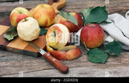 Die aus der Schale geschälten Äpfel liegen auf einem Holzbrett und einem Tisch. Erntezeit, Kochen zu Hause, Herbstfutter und Urlaub Stockfoto