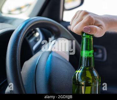 Eine gesichtslose Frau öffnet eine Flasche Bier, während sie mit dem Auto fährt. Gesetzesbruch und Alkoholkonsum während des Fahrens Stockfoto