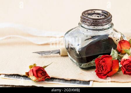 Tintenfass, Feder und getrocknete Rosen auf Vintage-Papier Hintergrund. Liebesbriefe Idee. Grüße zum Valentinstag. Stockfoto