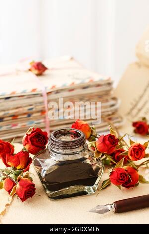 Tintenfass, Feder und getrocknete Rosen auf Vintage-Papier Hintergrund. Liebesbriefe Idee. Grüße zum Valentinstag. Stockfoto