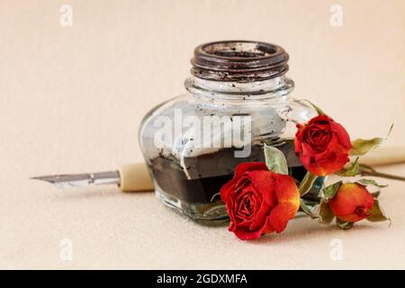 Tintenfass, Feder und getrocknete Rosen auf Vintage-Papier Hintergrund. Liebesbriefe Idee. Grüße zum Valentinstag. Stockfoto