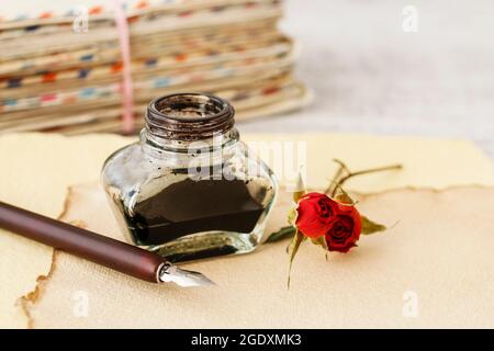 Tintenfass, Feder und getrocknete Rosen auf Vintage-Papier Hintergrund. Liebesbriefe Idee. Grüße zum Valentinstag. Stockfoto