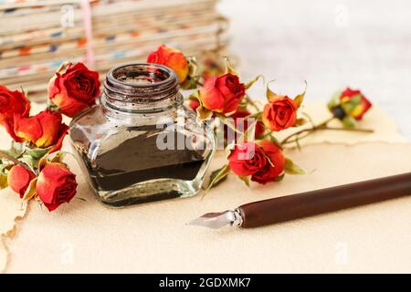 Tintenfass, Feder und getrocknete Rosen auf Vintage-Papier Hintergrund. Liebesbriefe Idee. Grüße zum Valentinstag. Stockfoto