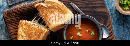 Blick von oben auf ein gegrilltes Käse-Sandwich, serviert mit einer Schüssel Tomatensuppe, fertig zum Essen. Stockfoto