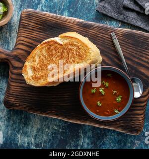 Blick von oben auf ein gegrilltes Käsesandwich mit Tomatensuppe auf einem Holzbrett. Stockfoto