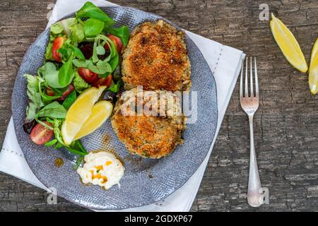 Sardinen-Fischkuchen mit grünem Blattsalat, Knoblauch-Mayo und Zitronenscheiben Stockfoto