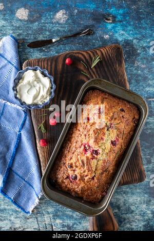 Draufsicht auf einen frisch aus dem Ofen gekühlten Preiselbeeren- und Rosmarinkuchen auf einem Holzbrett. Stockfoto