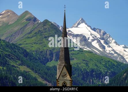 21. Juli 2021, Österreich, Heiligenblut: Die gotische Wallfahrtskirche in Heiligenblut ist dem Hl. Vinzenz von Saragossa geweiht und hinter dem Turm sieht man den schneebedeckten Gipfel des Großglockner. Der Großglockner ist 3,798 Meter hoch und damit der höchste Berg im Alpenraum Österreich. Es liegt im Zentrum des größten österreichischen Nationalparks hohe Tauern. Foto: Patrick Pleul/dpa-Zentralbild/ZB Stockfoto