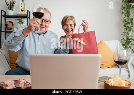 Seniorenpaar feiert Weihnachten auf Videoanruf virtuelle Party Essen und trinken Wein mit der Familie - Fokus auf Mann Gesicht Stockfoto
