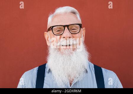 Porträt eines glücklichen Hipster-Senior-Mannes, der vor der Kamera lächelt, mit rotem Hintergrund - Fokus auf Gesicht Stockfoto