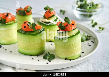 Urlaub Gemüse Vorspeisen. Gurkenbrötchen mit Weichkäse, gesalzenem Lachs, Microgreens und schwarzem Sesam auf einem weißen Teller serviert. Selecti Stockfoto