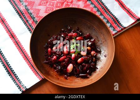 Traditioneller ukrainischer Salat mit Rote Beete und Bohnen - varya, serviert in der Tonschüssel auf dem traditionell bestickten Handtuch, Draufsicht Stockfoto