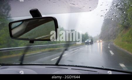 Blick auf den Straßenverkehr bei regnerischem Wetter aus dem Inneren eines Automobils. Konzept der Schlechtwetterfahrt Stockfoto