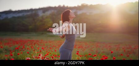 Junge schöne Frau mit erhobenen Armen im Frühjahr Mohnfeld. Sanfte Farben. Nachdenkliche, entspannte Atmosphäre. Stockfoto