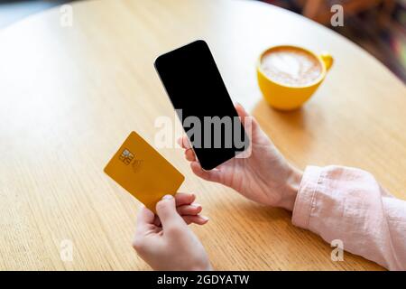 Kontaktlose Bezahlung während der Quarantäne des Coronavirus. Frau mit Handy und Kreditkarte, die Kaffee im Café trinkt Stockfoto