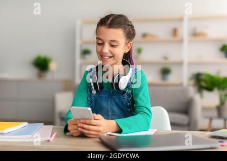 Mädchen sitzt am Schreibtisch und plaudert am Handy Stockfoto