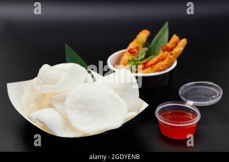 Krupuk oder chinesische traditionelle Chips mit Sauce und Garnelen in Tempura auf schwarzem Hintergrund. Junk-Food- oder Fastfood-Konzept. Reischips mit süßer und saurer oder würziger Chilisauce. Hochwertige Fotos Stockfoto