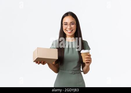 Lächelnd erfolgreiche junge weibliche Kleinunternehmen Eigentümer, Geschäftsfrau trinken Kaffee zum Mitnehmen und hält verpackt Box mit Kunden gekauft Artikel Stockfoto