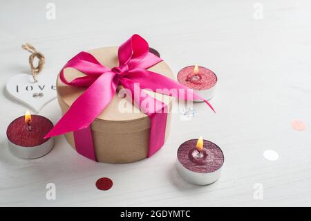 Geschenkbox mit rosa Schleife und brennenden Kerzen, Ansicht mit Kopierraum. Konzept der Valentinstag Urlaub Stockfoto