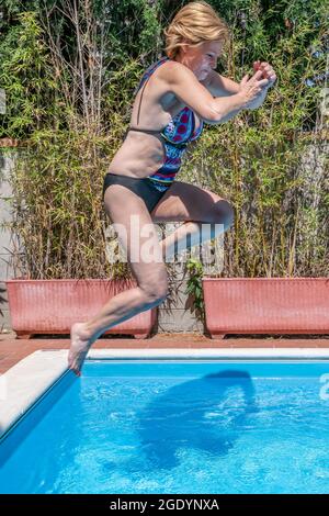 Eine weiße Frau mittleren Alters springt in einen Swimmingpool Stockfoto