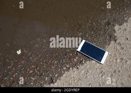 Mobiltelefon liegt auf dem Bürgersteig in der Pfütze. Stockfoto