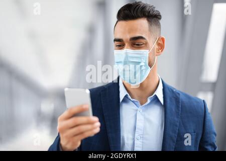 Arabischer Mann In Medizinischer Maske Mit Smartphone Während Der Wartezeit Im Flughafenterminal Stockfoto