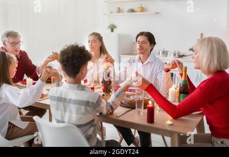 Große Familie mit mehreren Generationen hält sich die Hände und betet vor dem festlichen Abendessen zu Hause Stockfoto
