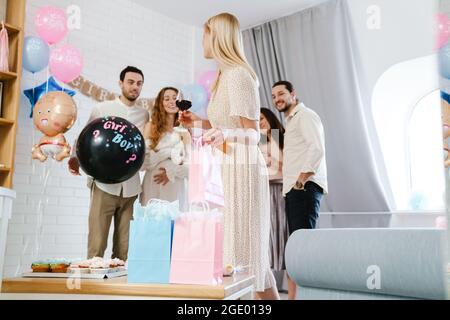 Junges glückliches Paar, das Geschenke von ihrer Freundin während der Geschlechtsenthüllung in Innenräumen annimmt Stockfoto