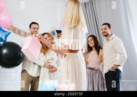 Junges glückliches Paar, das Geschenke von ihrer Freundin während der Geschlechtsenthüllung in Innenräumen annimmt Stockfoto