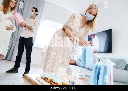 Junge, glückliche, schwanger Frau, die Geschenke von ihren Freunden während der Geschlechtsenthüllung in Innenräumen annimmt Stockfoto