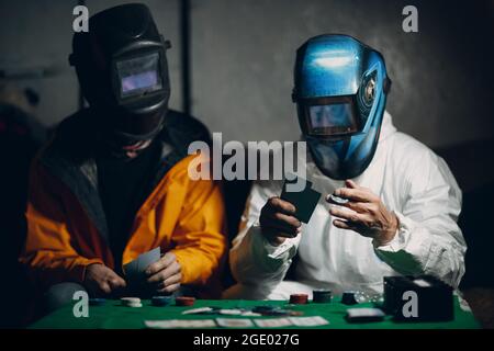 Zwei Schweißer in Schweißmasken spielen Poker Stockfoto