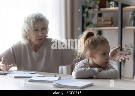 Unglückliche Großmutter und kleine Enkelin kämpfen mit Hausaufgaben Stockfoto