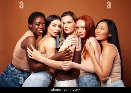Junge hübsche kaukasische, afro, skandinavische Frau posiert fröhlich zusammen auf braunem Hintergrund, Lifestyle diverse Nationalität Menschen Konzept Stockfoto