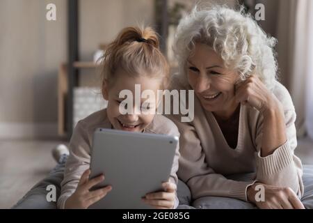 Glückliche alte Oma und kleine Enkelin verwenden Tablet Stockfoto