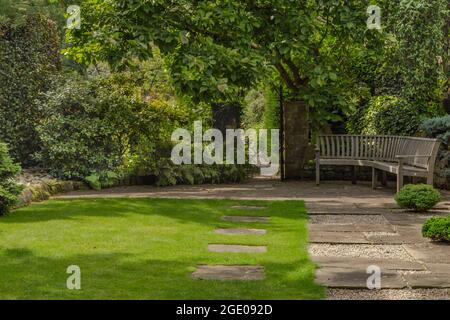 Ein Pfad über einen Rasen, der zu einem offenen Tor im York Gate Garden, Leeds, Yorkshire, England führt. Stockfoto