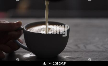 Gießen Sie gestreamte Milch in eine blaue Tasse, um Cappuccino mit Platz zum Kopieren und breitem Foto zuzubereiten Stockfoto