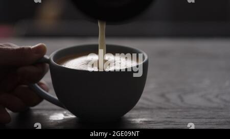 Gießen Sie gestreamte Milch in eine blaue Tasse, um Cappuccino mit Platz zum Kopieren und breitem Foto zuzubereiten Stockfoto