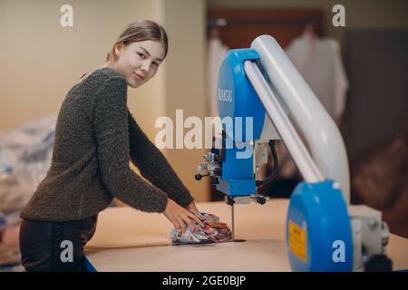 Junge schöne Schneiderin Kleidung Designer schneidet Stoff auf der Maschine. Stockfoto