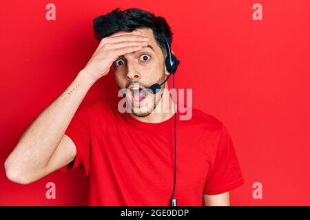 Junger hispanischer Mann mit Headset für Callcenter-Agenten gestresst und frustriert, mit der Hand auf dem Kopf, überrascht und wütend im Gesicht Stockfoto