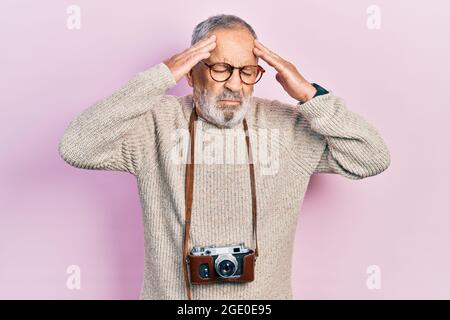 Hübscher älterer Mann mit Bart, der die Vintage-Kamera mit der Hand am Kopf hält, Kopfschmerzen wegen Stress. Migräne. Stockfoto