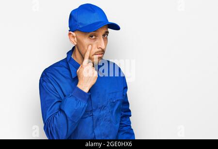 Glatze Mann mit Bart tragen Baumeister Jumpsuit Uniform zeigt auf das Auge beobachten Sie Geste, verdächtiger Ausdruck Stockfoto