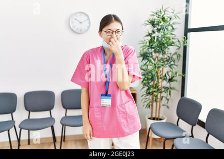 Junge asiatische Krankenschwester Frau im medizinischen Wartezimmer riecht etwas stinkend und ekelhaft, unerträglichen Geruch, Atem mit den Fingern auf der Nase halten. Schlecht Stockfoto