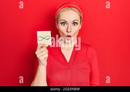 Junge blonde Frau hält unendliche Symbol Erinnerung erschrocken und erstaunt mit offenem Mund für Überraschung, Unglauben Gesicht Stockfoto