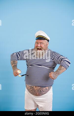 Schneidig plus Größe Person trägt Seemann Kostüm mit Pfeifenposen auf hellblauem Hintergrund Stockfoto