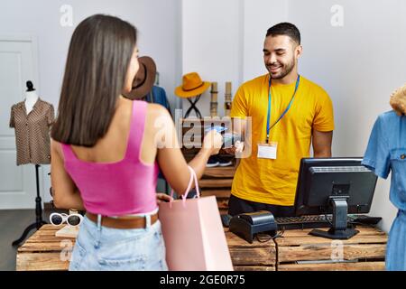 Junger mann aus lateinamerika, der im Bekleidungsgeschäft mit Kreditkarte an den Ladenbesitzer zahlt. Stockfoto