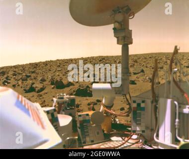 Viking 2 Bild der Mars-Utopien-Ebene Beschreibung: Das mit Steinen übersäte Feld aus roten Felsen reicht bis zum Horizont, fast zwei Meilen von Viking 2 auf der Mars-Utopien-Ebene entfernt. Wissenschaftler glauben, dass die Farben der Marsoberfläche und des Himmels auf diesem Foto ihre wahren Farben repräsentieren. Feine Partikel aus rotem Staub haben sich auf den Oberflächen der Raumfahrzeuge niedergelassen. Die Lachsfarbe des Himmels wird durch Staubpartikel verursacht, die in der Atmosphäre schweben. Die Farbkalibrierungstabellen für die Kameras sind an drei Stellen auf dem Raumschiff montiert. Beachten Sie das blaue Sternfeld und die roten Streifen der Flagge. Stockfoto