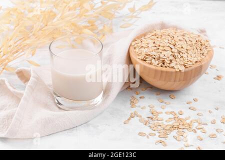 Vegane, nicht milchfreie Alternativmilch. Glas mit Hafermilch und eine Schüssel mit Haferflocken auf dem Tisch aus weißem Stein, Nahaufnahme Stockfoto