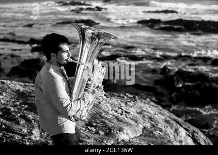 Ein Mann mit einer Tuba am Meer. Schwarzweiß-Foto. Stockfoto