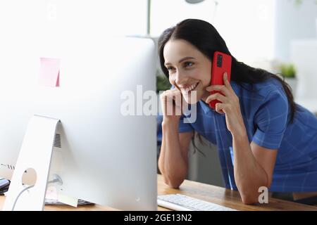 Fröhliche Frau, die am Handy spricht und auf den Computerbildschirm schaut Stockfoto